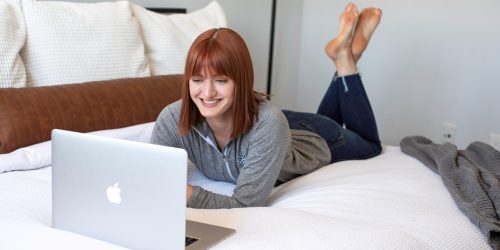smiling business owner laying on bed reviewing customer personalization results on computer